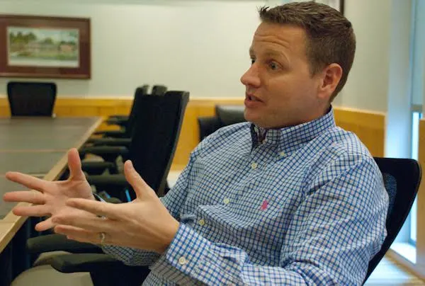 Chuck Norman, business owner, engaged in discussion, gesturing with his hands at a conference table, wearing a blue and white checkered shirt